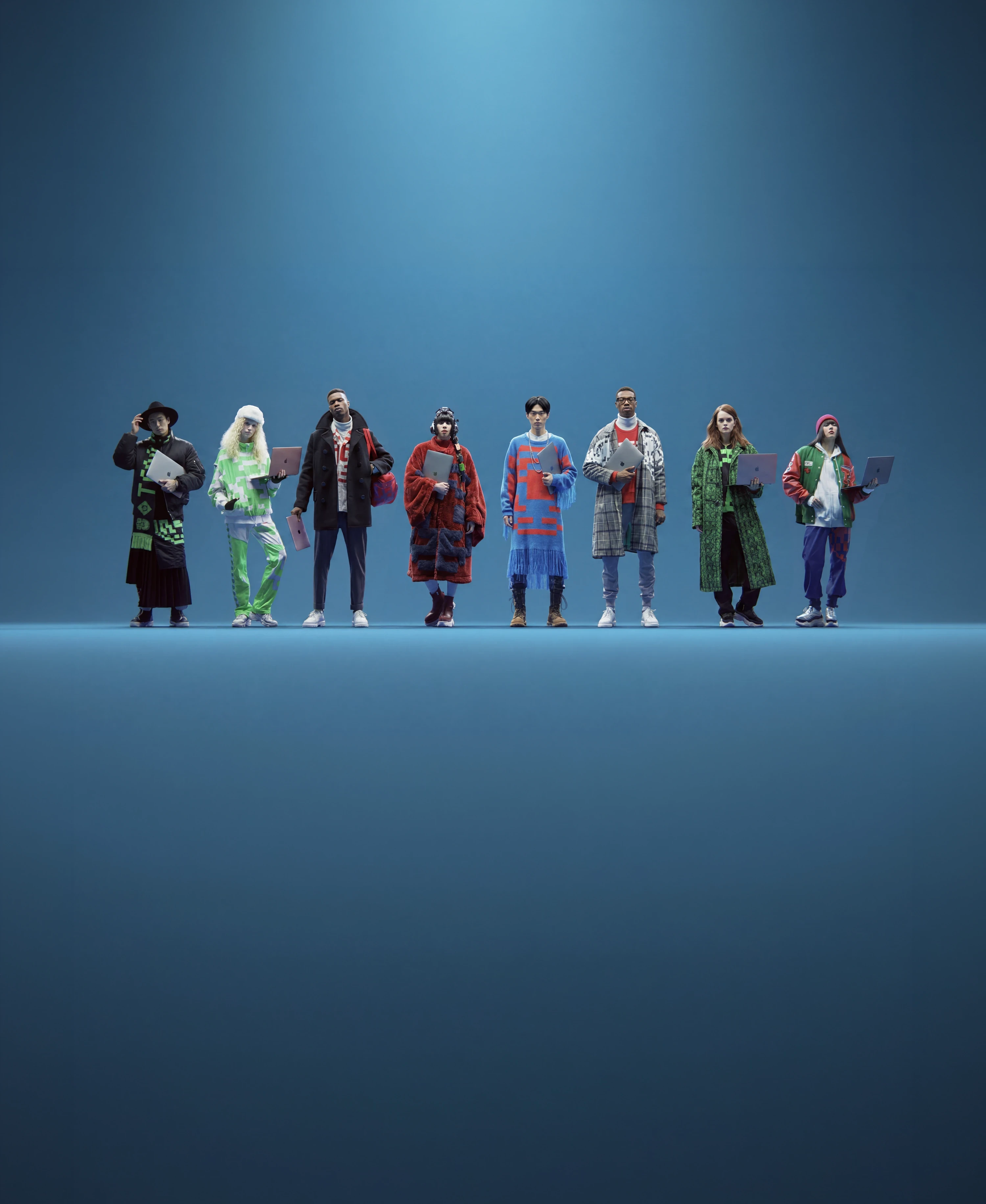 Eight production-team members standing in a row, each holding a laptop, on a blue studio background